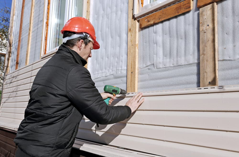 A worker installing siding on a house