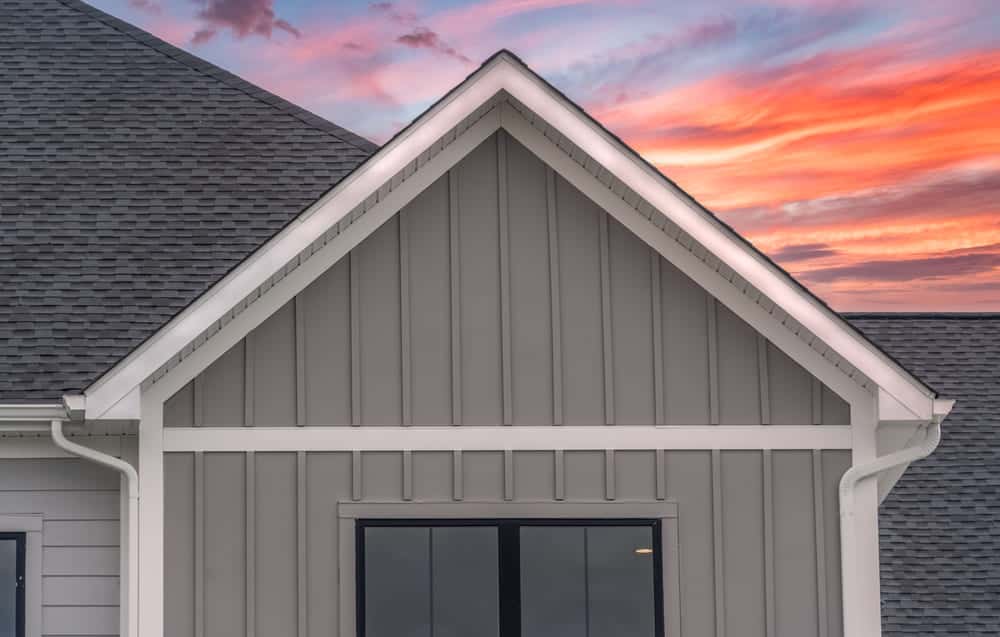 White frame gutter guard system, with dark gray horizontal vinyl siding. White accents, fascia, soffit, on a pitched roof attic. A luxury American single family home dramatic colorful sunset sky.