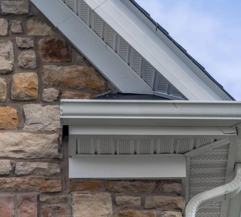 Gable with colored stone siding, white frame gutter guard system, fascia, drip edge. House soffit on a pitched roof attic at a luxury American single-family home.